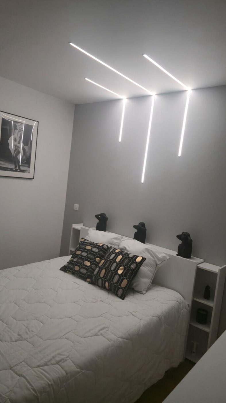 Chambre éclairée par trois profilés LED encastrés affleurants, filant du plafond puis descendant le long du mur